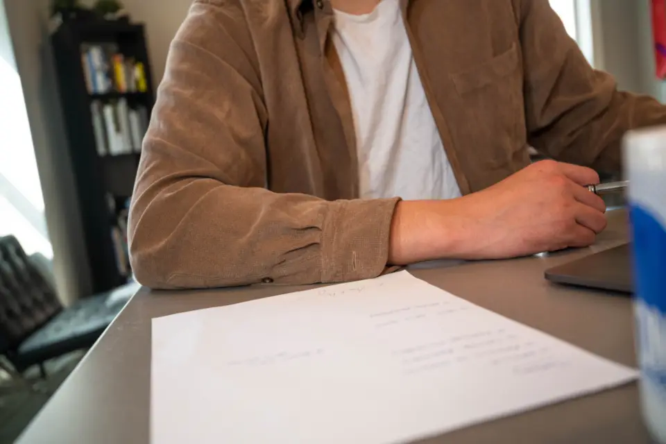 Business owner at a desk with a pen in hand, about to sign a typed one-page letter beside a laptop